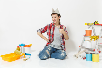 Happy fun woman in newspaper hat sitting on floor with instruments for renovation apartment room...