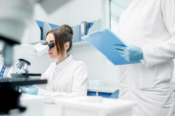 Medics in uniform working with microscope making analysis at the laboratory office