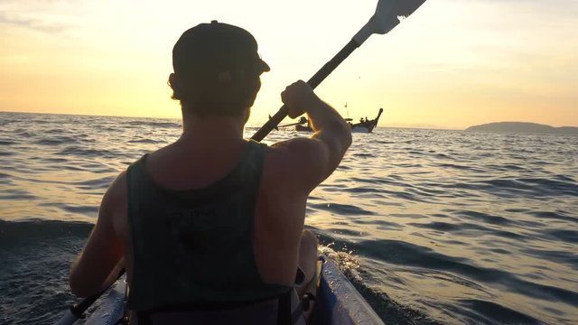 Back View of Strong Man on Kayak in the Open Sea Water. Sunset over the Rock Cliffs. Railey Beach, Krabi, Thailand.