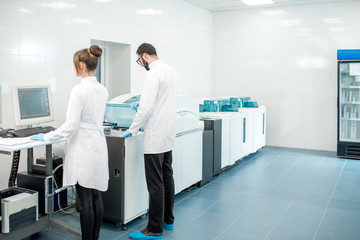 Couple of medics configuring analyzer machine in the modern laboratory