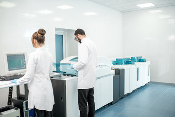 Couple of medics configuring analyzer machine in the modern laboratory