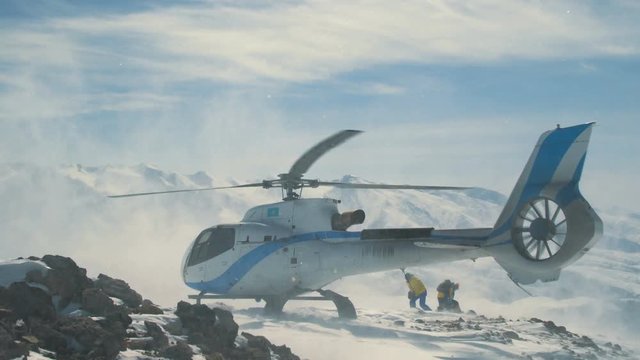 Heliskiing helicopter landed in the snow mountains, raising a big cloud of snow