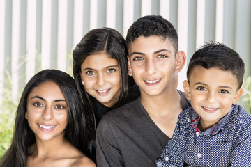 Smiling siblings in garden. Outdoor portrait of two brothers and two sisters, blurred white fence background.
