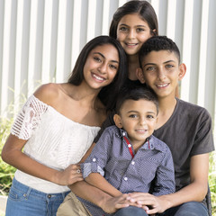 Smiling siblings in garden. Outdoor portrait of two brothers and two sisters, blurred white fence background.