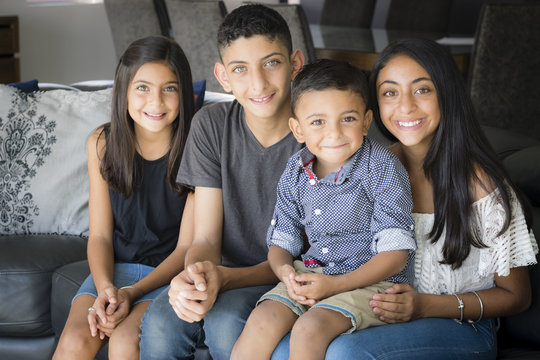 Smiling siblings in the living room. Two brothers and two sisters sitting on the couch smiling.