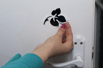 The girl glues the cut out elements from self-adhesive paper, to mask the defects of the white door.