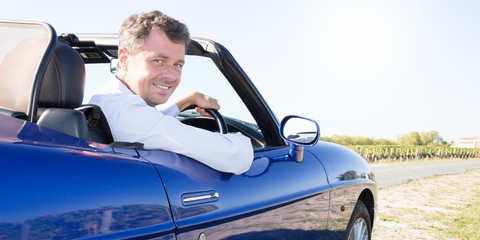 Elegant young happy man in blue convertible car outdoors summer country side