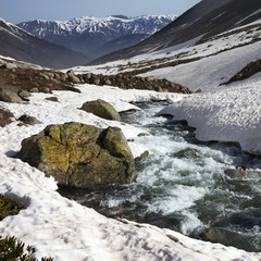 River with snow bridges in mountains at sun day