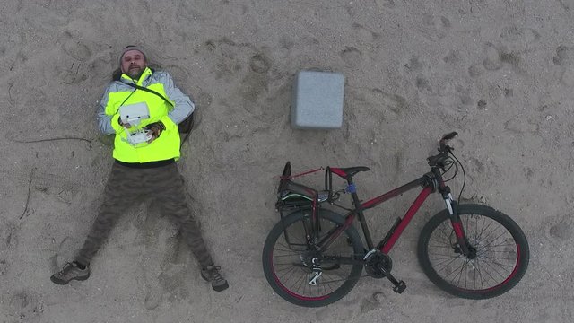 Aerial view mature man with a beard lies on sand with a control panel for drone