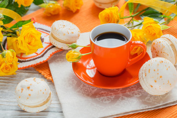 Orange cup of black coffee, yellow roses flowers and sweet pastel french macaroons
