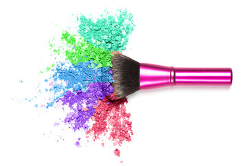 Crumbled colourful eyeshadow splash with brush on white isolated background.