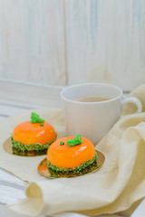 Bright orange mousse cakes and cup of coffee on white wooden tray