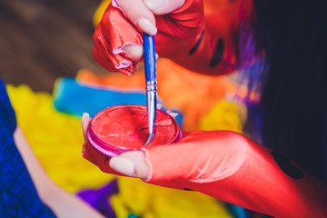 Drawing a face painting on a girl's face. Painter's brushes and hands