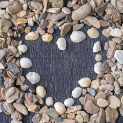 Heart made of sea shells and gravel over wooden textured background, closeup. Romance and tropical holiday concept.