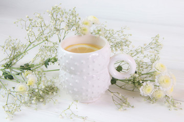 white cup of herbal tea and lemon with white flowers on a wooden background