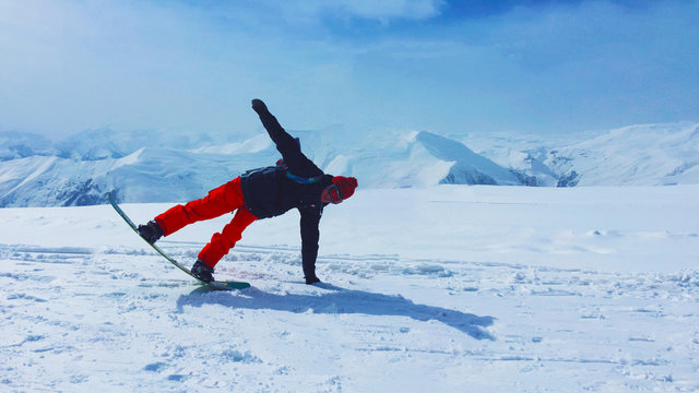 Man On A Snow Board Leaning Into A Curve With A Picturesque Alpine Background. Snowboarder Racing Downhill On A Sunny Day.