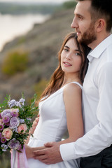 Obraz premium newly marriage beautiful couple, bride and groom, standing with wedding bouquet near river and mountains. Close-up