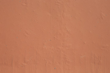 Front close-up view of a cement wall painted in light brown color. There are some particles stuck under the paint layer and brush trails can be clearly seen as well.
