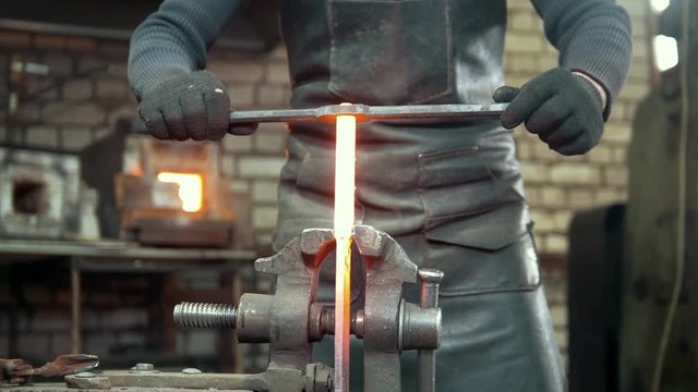 Muscular blacksmith in forge hammering steel products