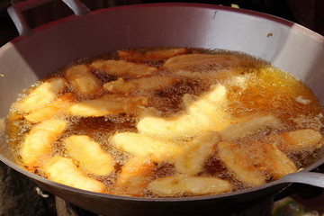 Cooking bananas in batter are fried in a aluminum bowl with boiling vegetable oil on Asian street market.