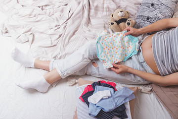 Fototapeta premium Pregnant woman with various clothes for a newborn
