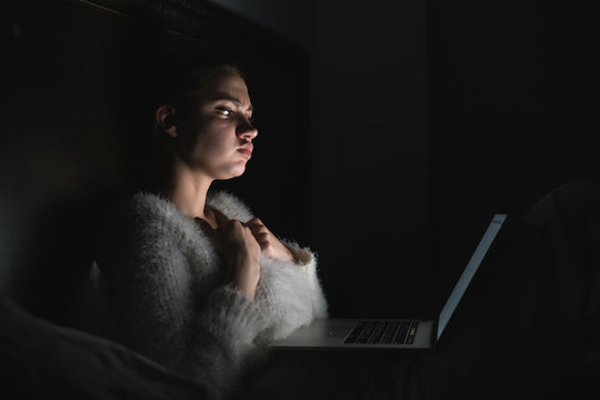 Young Girl Sits In The Dark At Night Watching A Horror Film On Her Laptop