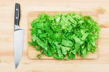Close-up on a wooden table is a wooden cutting board on which lies chopped lettuce leaves and next...