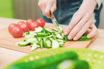 close-up of female hands cut into fresh cut cucumbers on a wooden cutting board next to pink tomatoes. The concept of homemade vegetarian cuisine and healthy eating and lifestyle