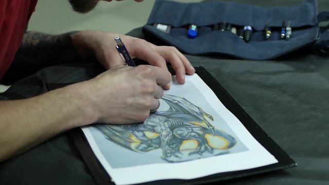 Tattoo master draw picture of dragon, tattooer work in studio