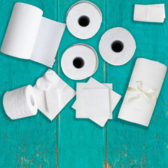 Paper tissue, white toilet  paper rolls, towels, napkins, cotton pads stacked on rustic wooden aquamarine table. Copy space. Top view.