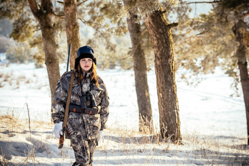 female hunter in camouflage clothes ready to hunt, holding gun and walking in forest. hunting and people concept