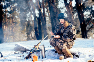 Female hunter preparing food with a portable gas burner in a winter forest. Bushcraft, hunting and...