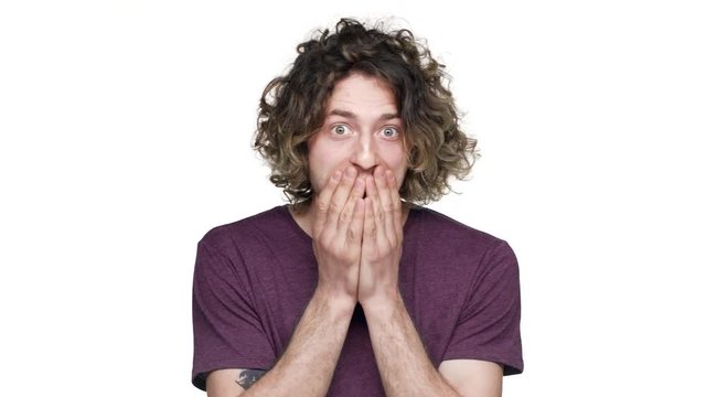 Portrait of young guy with curly hair in casual t-shirt covering face in surprise and expressing delight, isolated over white background. Concept of emotions