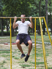 Young man exercising on horizontal bar outdoors