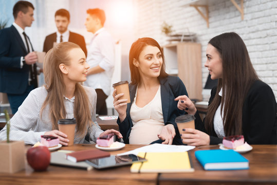 Three Young Beautiful Girls Socialize Drinking Coffee And Eating Cakes In The Office.