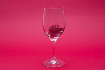Ripe strawberries in a wine glass on red background