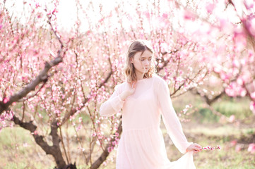 Spring portrait og blonde girl in blooming peach orchard. Spring season. 20s.