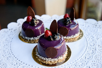 Tasty violet cakes with berries stand on white tablecloth