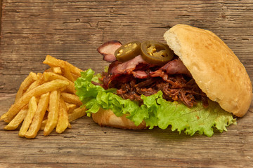 Barbeque Pulled beff Sandwich with green salad,crisp bacon,hot pepper jalapeno,BBQ Sauce and Fries on wooden background,Fast food