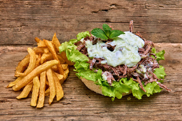Barbeque Pulled Pork Sandwich with green salad,Tzatziki Sauce,BBQ Sauce and Fries on wooden background