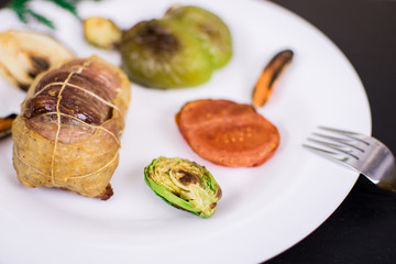 Cutlet from meat with grilled vegetables on a white plate and against a dark background.