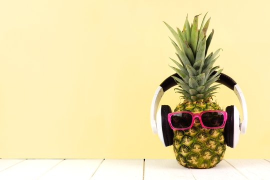 Hipster pineapple with sunglasses and headphones against a yellow background. Minimal summer concept.