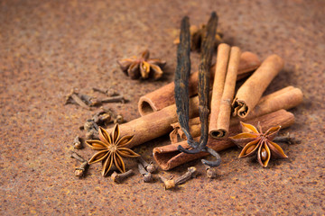 Vanilla, cinnamon and other spices on a rusty table.