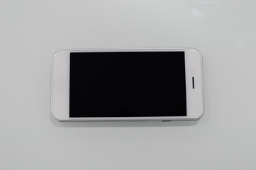 Top view on white smartphone with mockup screen on light table background. Close up with copy space, modern communication technology flat lay design