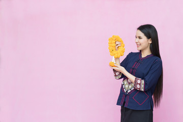 Portrait of asian young girl in traditional thai dress and holding  marigold garland isolated on pink background. Cotton dress