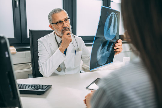 Mature doctor examining the medical x-rays image in hospital office.