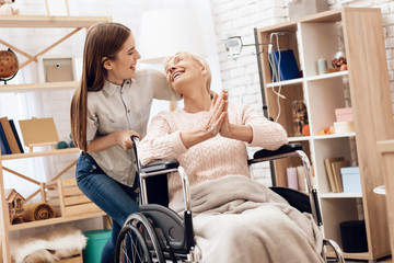 Obraz premium Girl is nursing elderly woman at home. Girl is riding woman in wheelchair. Woman is enjoying herself.