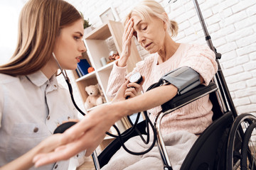 Girl is caring for elderly woman at home. Girl is checking blood pressure with tonometer.