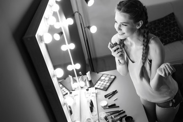 Portrait of beautiful woman with natural makeup applying perfume near mirror indoors, black and white effect
