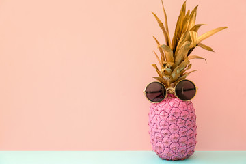 Pink pineapple with sunglasses on color background
